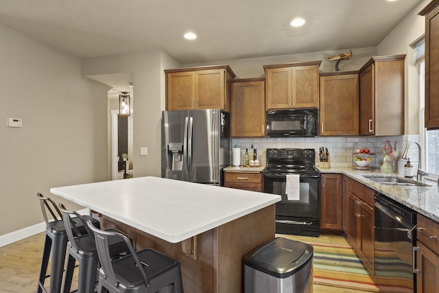 kitchen with backsplash, a kitchen island, a sink, light wood-type flooring, and black appliances