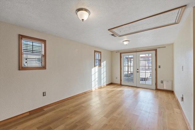 empty room featuring light hardwood / wood-style flooring, a textured ceiling, and french doors