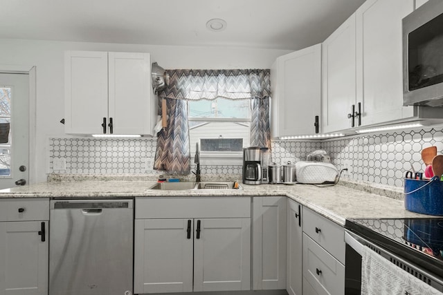 kitchen with appliances with stainless steel finishes, tasteful backsplash, white cabinetry, sink, and light stone counters