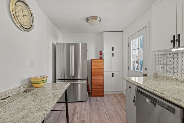 kitchen featuring appliances with stainless steel finishes, tasteful backsplash, white cabinetry, light stone counters, and light hardwood / wood-style flooring