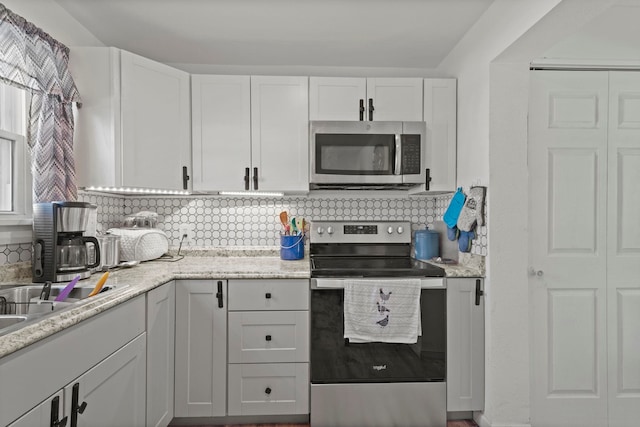 kitchen featuring stainless steel appliances, white cabinets, light stone counters, and decorative backsplash