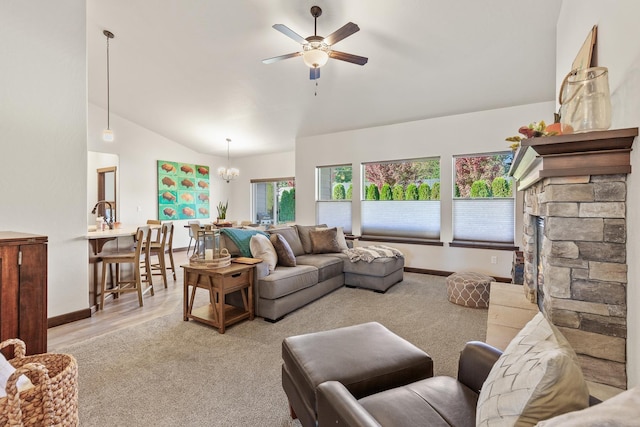 living room with a stone fireplace, ceiling fan with notable chandelier, and vaulted ceiling