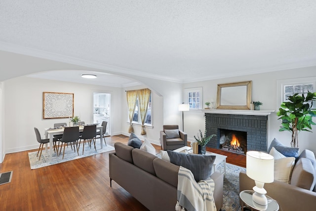 living room with a brick fireplace, crown molding, a textured ceiling, and a healthy amount of sunlight