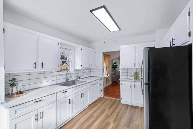 kitchen with stainless steel refrigerator, tasteful backsplash, white cabinetry, sink, and light wood-type flooring