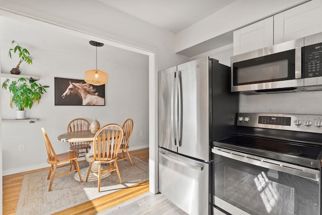 kitchen with white cabinetry, stainless steel appliances, hanging light fixtures, and light wood-type flooring