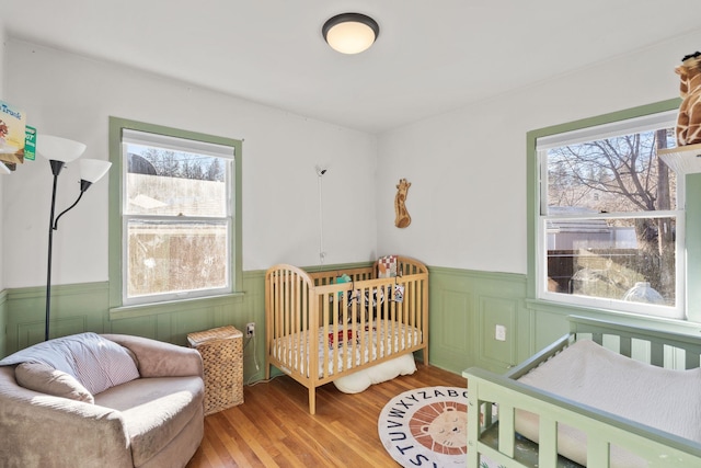 bedroom featuring multiple windows, a crib, and wood-type flooring