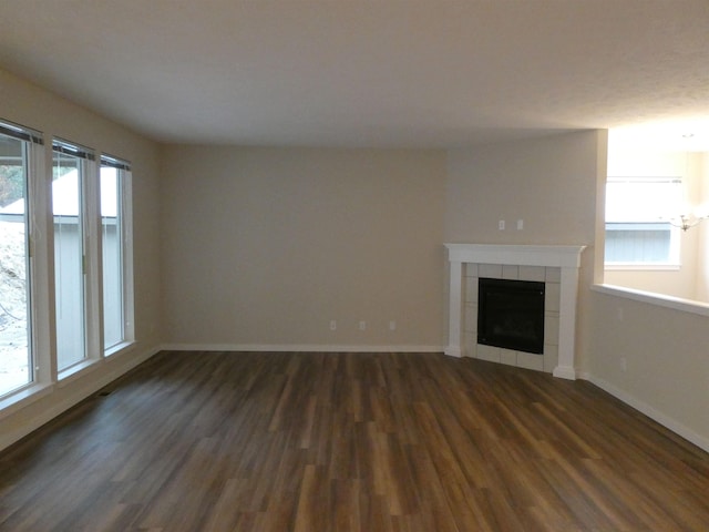 unfurnished living room featuring a tiled fireplace and dark hardwood / wood-style flooring