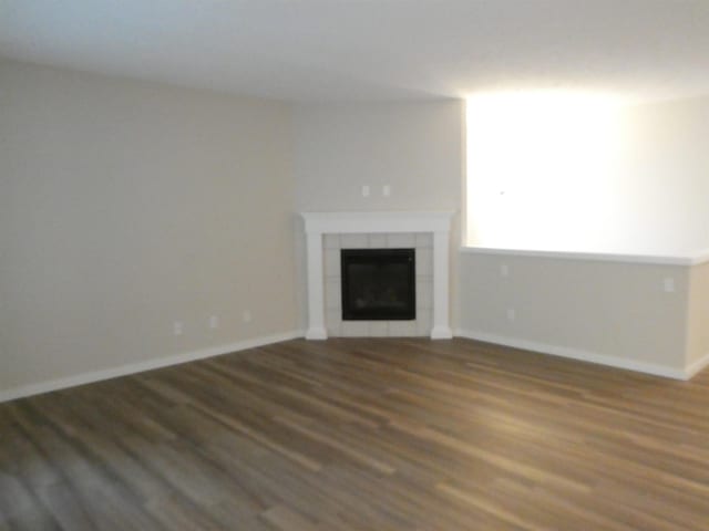 unfurnished living room with dark wood-type flooring and a tiled fireplace