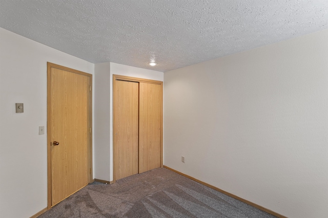 unfurnished bedroom featuring a textured ceiling, dark carpet, and a closet