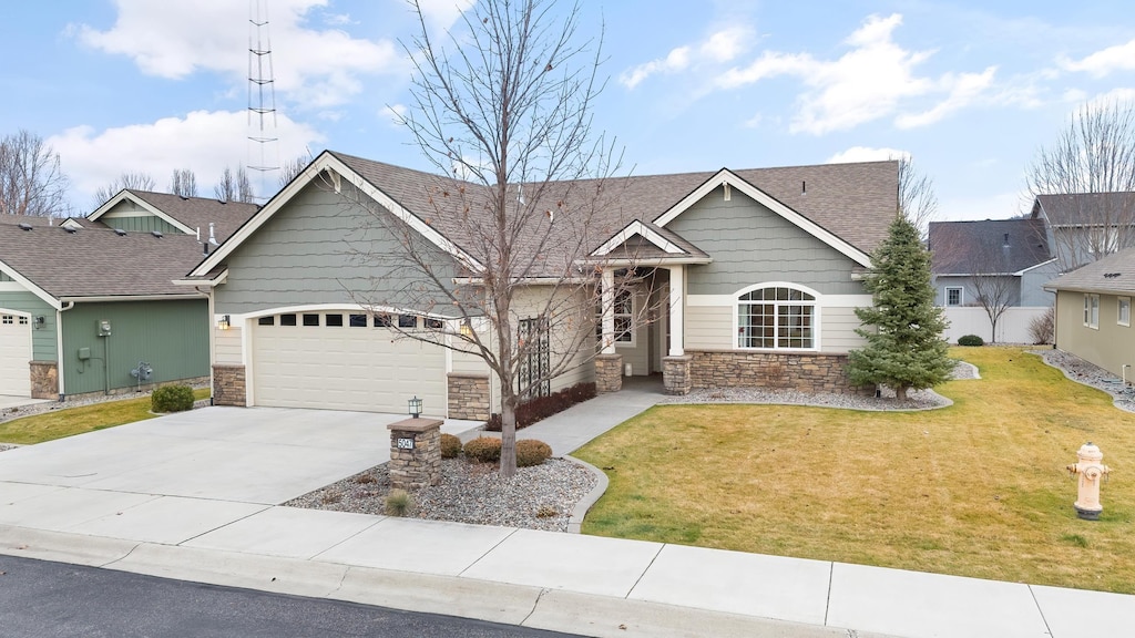 view of front of home with a shingled roof, a front yard, a garage, stone siding, and driveway