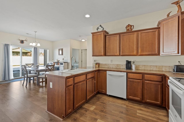 kitchen with sink, decorative light fixtures, kitchen peninsula, hardwood / wood-style flooring, and white appliances