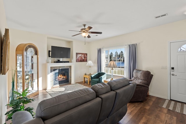 living room featuring ceiling fan, dark hardwood / wood-style flooring, and a tiled fireplace