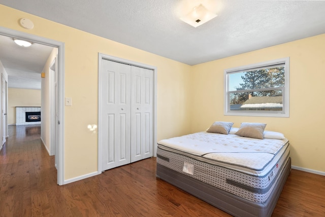 bedroom featuring dark wood-type flooring, a fireplace, a closet, and a textured ceiling