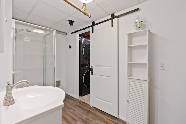 bathroom featuring hardwood / wood-style flooring, stacked washer / drying machine, sink, and a drop ceiling