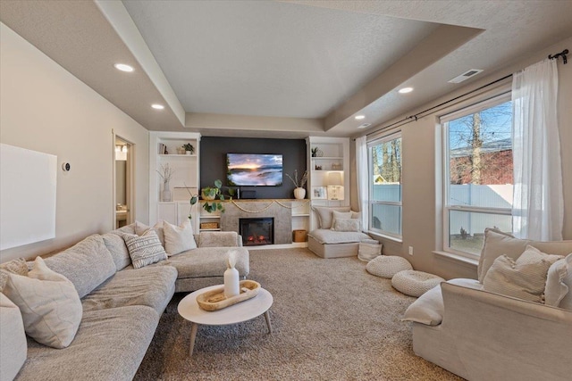 carpeted living room with built in shelves, a raised ceiling, and a textured ceiling