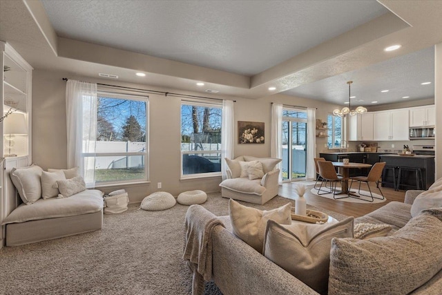 living room featuring an inviting chandelier, a tray ceiling, carpet floors, and a textured ceiling