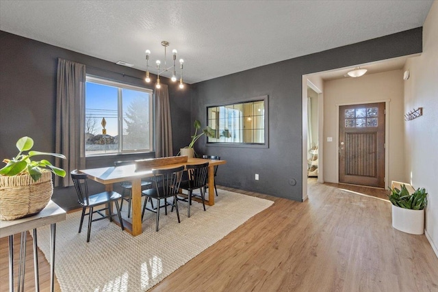 dining room featuring a notable chandelier, plenty of natural light, a textured ceiling, and light wood-type flooring