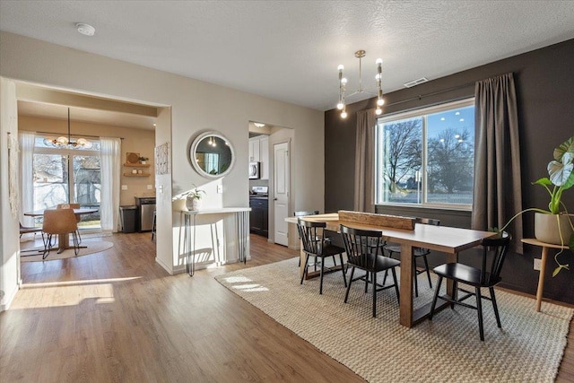 dining area featuring a healthy amount of sunlight, hardwood / wood-style floors, a textured ceiling, and a notable chandelier