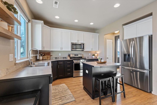 kitchen with sink, stainless steel appliances, a center island, white cabinets, and a kitchen bar