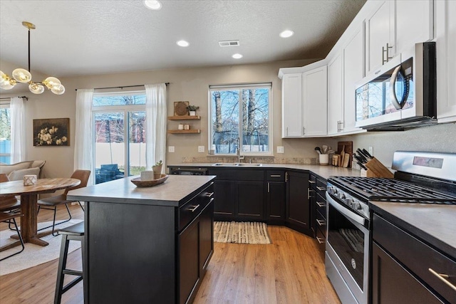 kitchen with sink, white cabinetry, a center island, hanging light fixtures, and stainless steel appliances