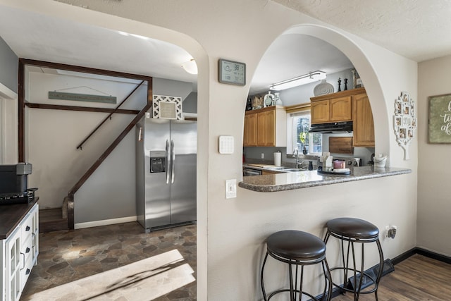 kitchen featuring stainless steel refrigerator with ice dispenser, a kitchen bar, sink, a textured ceiling, and kitchen peninsula