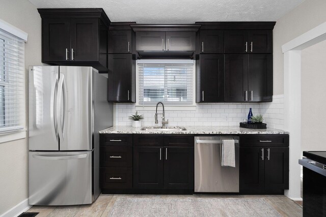 kitchen with light stone counters, sink, decorative backsplash, and appliances with stainless steel finishes