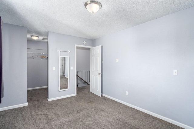 unfurnished bedroom with a spacious closet, carpet flooring, a closet, and a textured ceiling