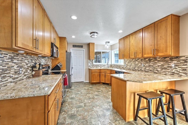 kitchen with appliances with stainless steel finishes, sink, a kitchen bar, decorative backsplash, and kitchen peninsula