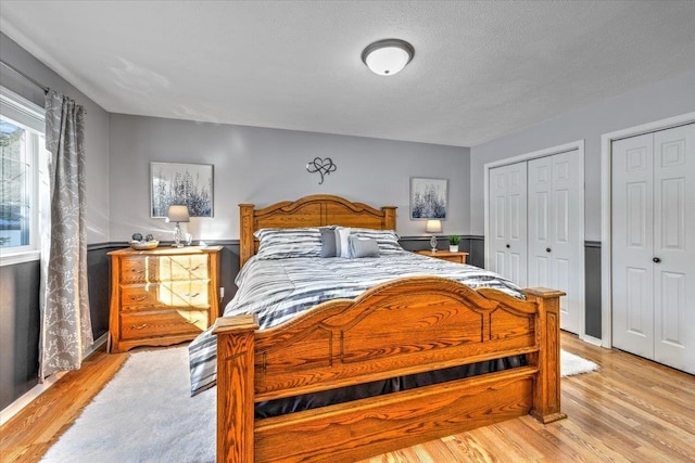 bedroom featuring multiple closets, a textured ceiling, and light wood-type flooring