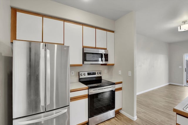 kitchen with stainless steel appliances, white cabinets, and light hardwood / wood-style floors