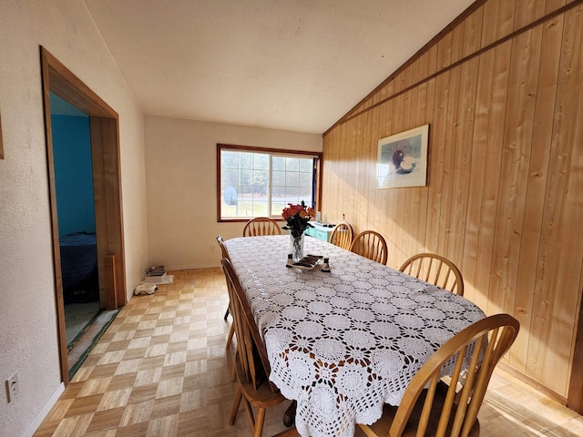 dining area with light parquet floors, lofted ceiling, and wood walls