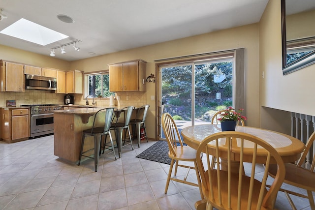 kitchen with sink, a skylight, appliances with stainless steel finishes, kitchen peninsula, and backsplash