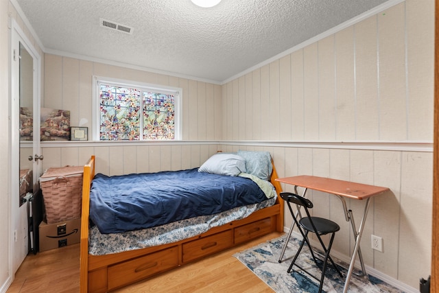 bedroom featuring ornamental molding, light hardwood / wood-style floors, and a textured ceiling