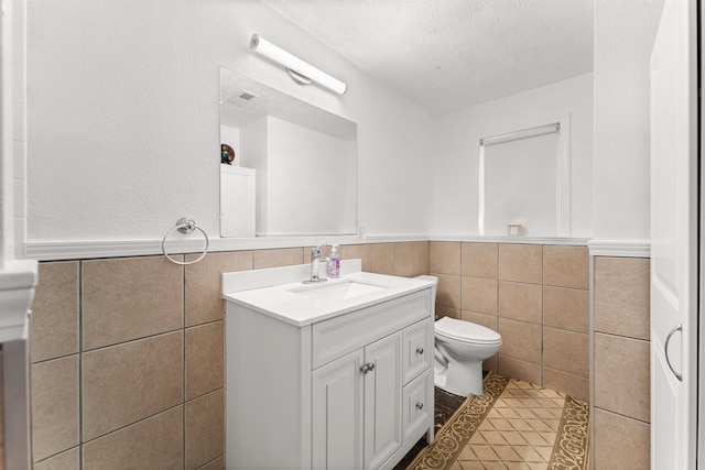 bathroom with tile walls, vanity, toilet, tile patterned floors, and a textured ceiling