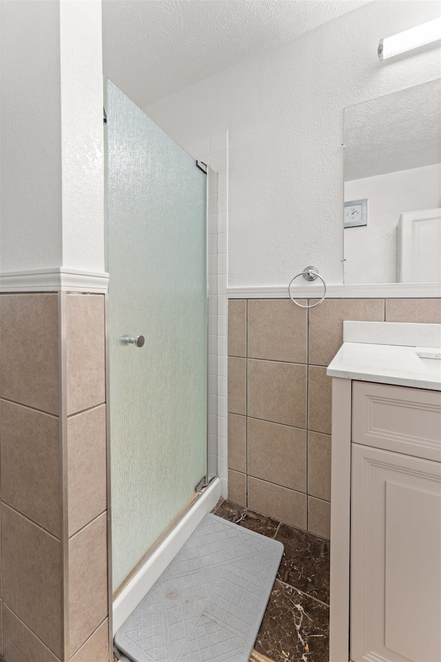 bathroom featuring an enclosed shower, vanity, tile walls, and a textured ceiling