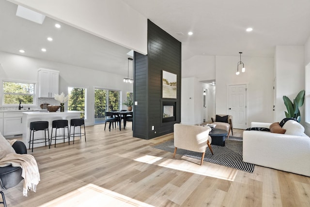 living room featuring a multi sided fireplace, light wood-type flooring, sink, and high vaulted ceiling