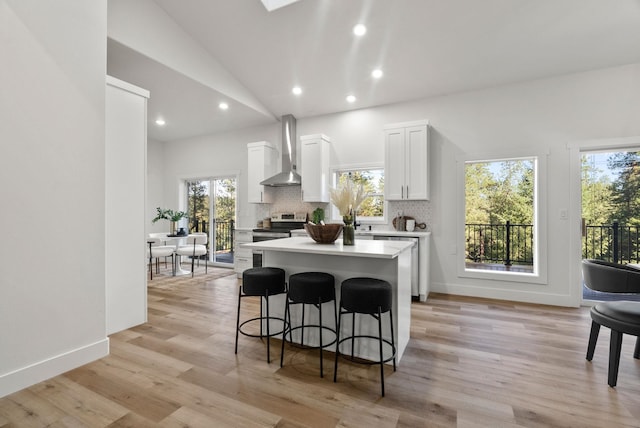 kitchen with white cabinetry, a breakfast bar area, a center island, stainless steel appliances, and wall chimney range hood