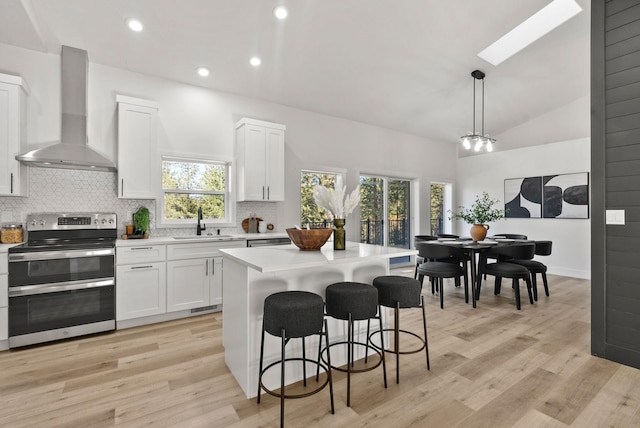 kitchen featuring white cabinetry, double oven range, a kitchen island, pendant lighting, and wall chimney range hood