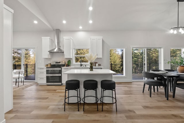 kitchen with wall chimney range hood, sink, white cabinetry, double oven range, and decorative light fixtures