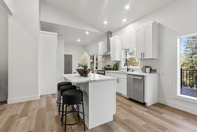 kitchen featuring sink, appliances with stainless steel finishes, a kitchen island, wall chimney range hood, and white cabinets