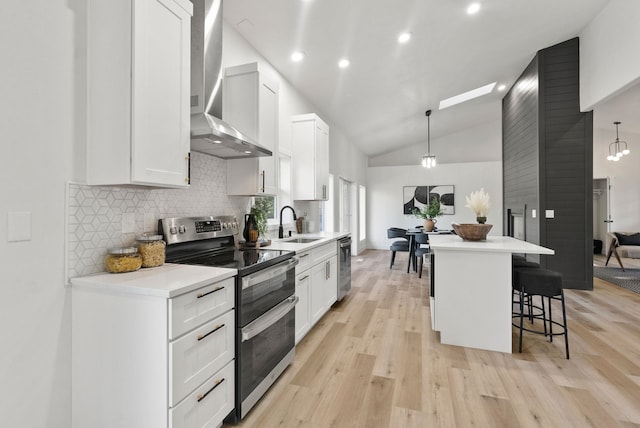 kitchen featuring white cabinetry, decorative light fixtures, a center island, appliances with stainless steel finishes, and wall chimney range hood