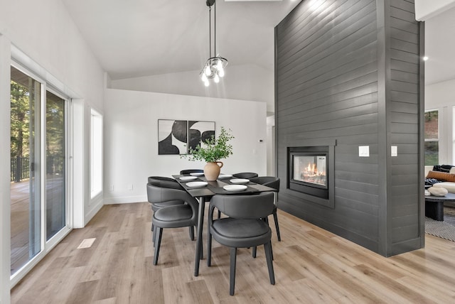 dining area featuring a fireplace, high vaulted ceiling, and light wood-type flooring