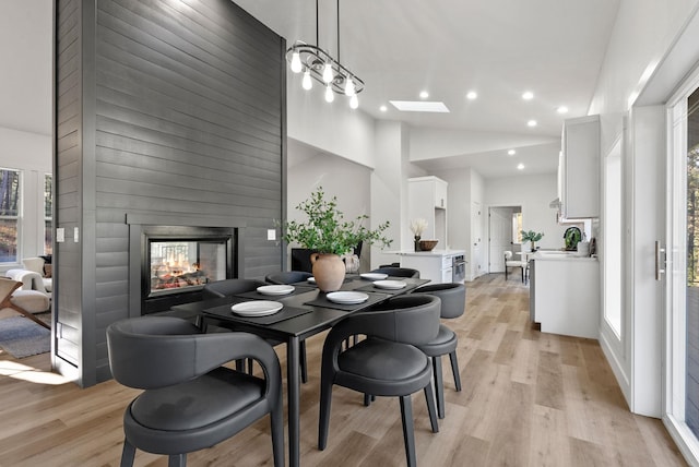 dining room featuring light wood-type flooring, high vaulted ceiling, plenty of natural light, and a multi sided fireplace