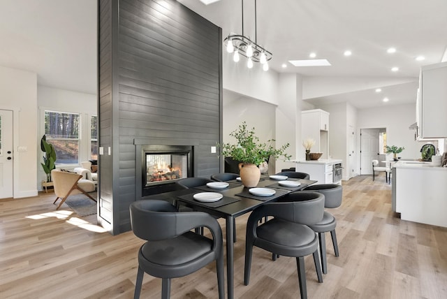 dining space featuring sink, light hardwood / wood-style floors, high vaulted ceiling, and a multi sided fireplace