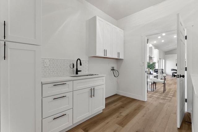 interior space featuring sink, white cabinetry, tasteful backsplash, vaulted ceiling, and light wood-type flooring