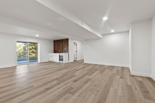 unfurnished living room with bar, beverage cooler, and light wood-type flooring