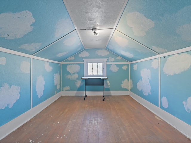 additional living space featuring hardwood / wood-style floors, vaulted ceiling, and a textured ceiling