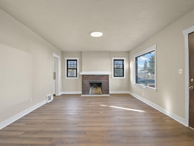 unfurnished living room featuring a brick fireplace and dark wood-type flooring