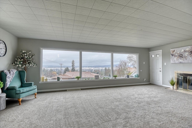 unfurnished living room featuring a healthy amount of sunlight, carpet, baseboards, and a fireplace with flush hearth