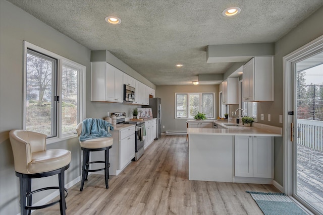 kitchen featuring stainless steel appliances, light countertops, white cabinets, a sink, and a peninsula